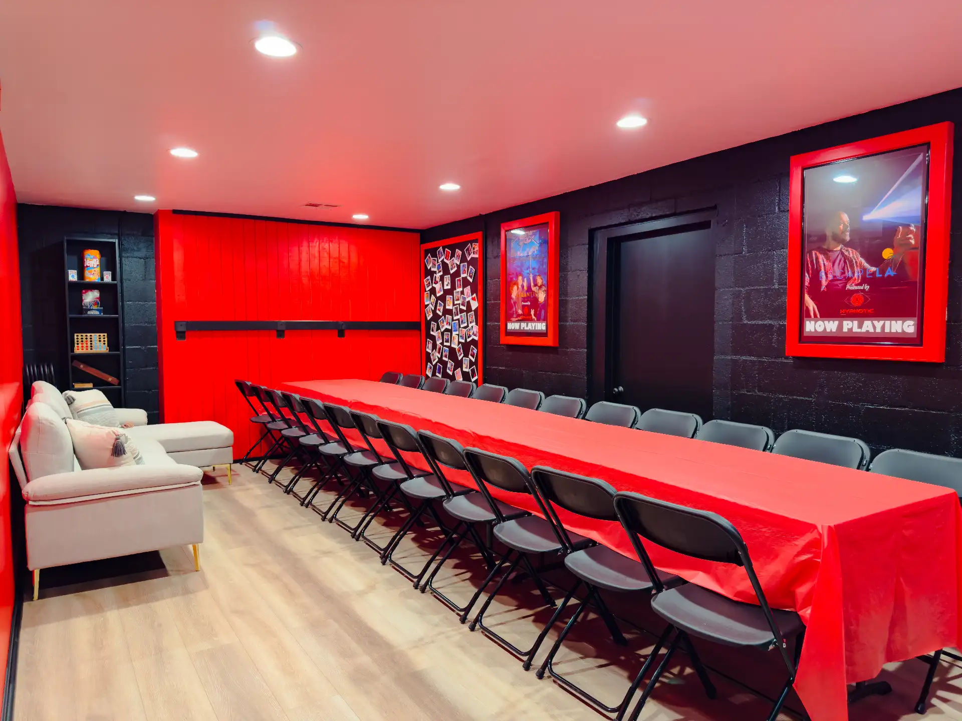 The private party room set for a group — a long red-clothed banquet table lined with chairs, a white lounge sofa at the near end, and framed escape-room posters along the wall