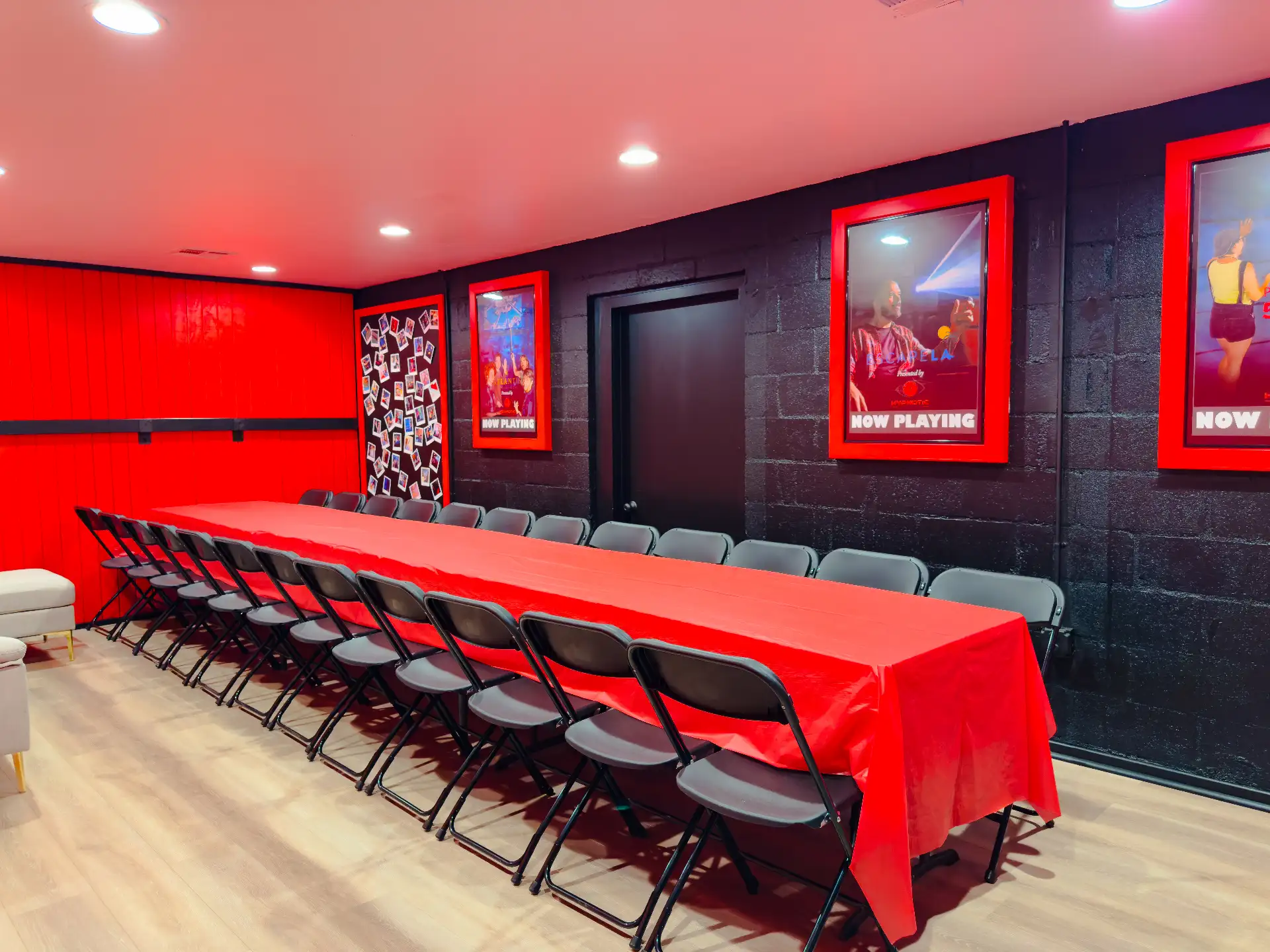 Folding chairs lined down both sides of the red banquet table under the poster wall