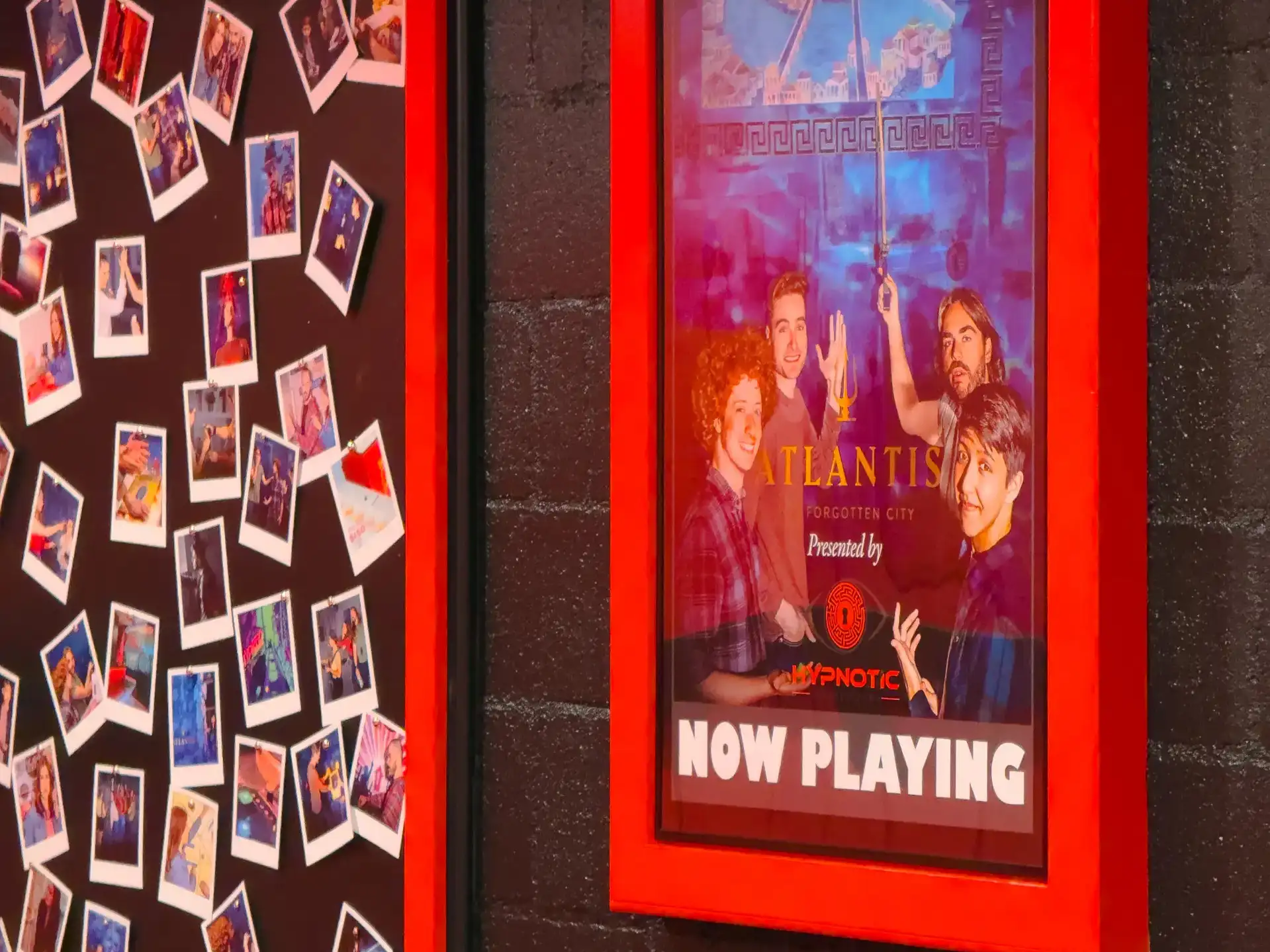 A wall of polaroids of past players beside a framed 'Atlantis — Now Playing' poster in the party room