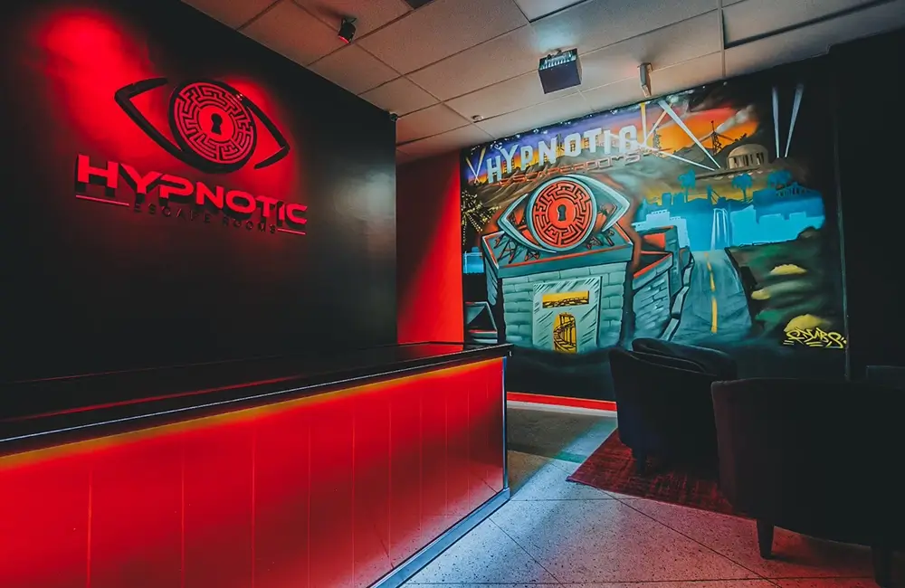 The lobby's backlit Hypnotic Escape Rooms logo wall beside the painted arcade mural