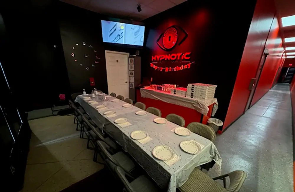 The lobby set for a birthday party — table settings, wall-mounted screens, and the lit logo wall behind