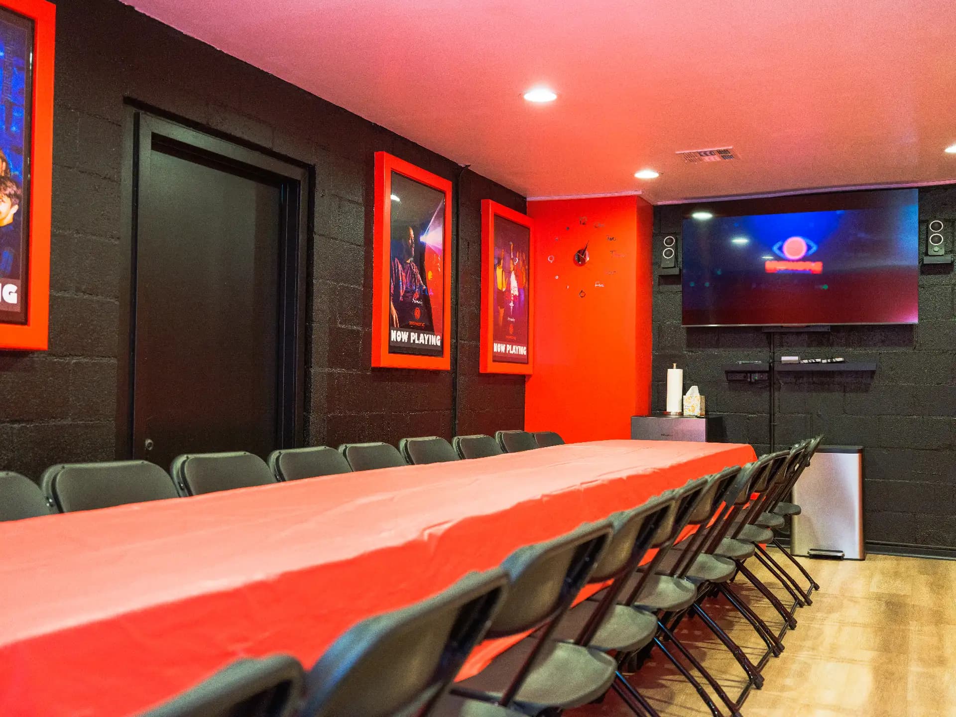 A low view along the red banquet table toward the wall-mounted screen at the far end of the party room
